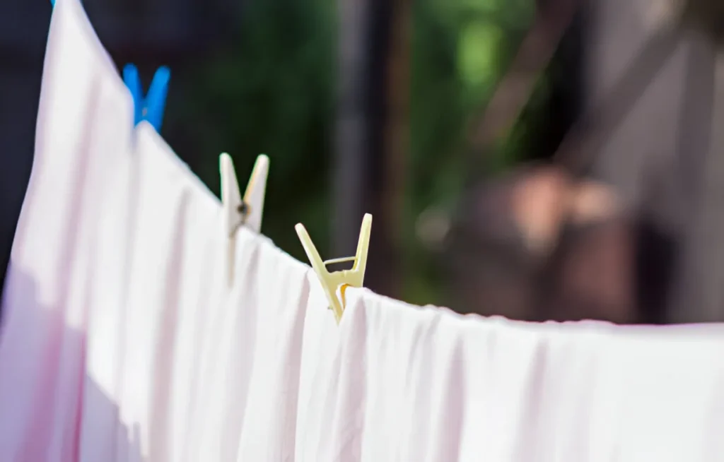 The clean cotton bed sheets are hung on the rope outside to dry